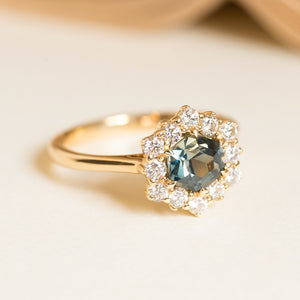 Teal sapphire engagement ring set with a hexagon-cut sapphire framed by a sparkling diamond cluster in yellow gold.