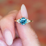 Teal sapphire and diamond cluster tre-foil engagement ring with brilliant teal sapphire and diamond side stones.