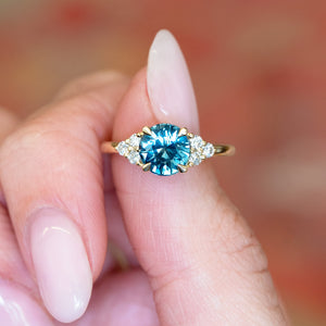 Teal sapphire and diamond cluster tre-foil engagement ring with brilliant teal sapphire and diamond side stones.