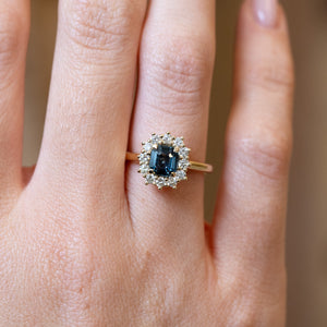 Close detail of teal sapphire and diamond cluster engagement ring with diamond halo.