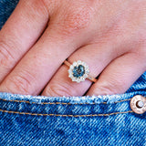 Teal sapphire cluster ring worn on hand with denim pocket detail.