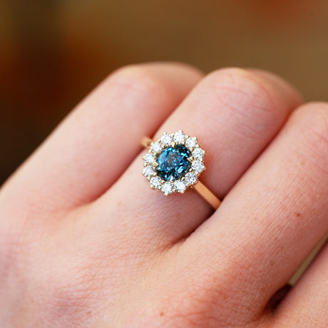 Close up of a teal sapphire ring with diamond halo showing deep blue green tone and sparkle.