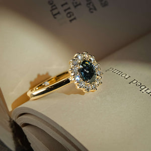 Teal sapphire engagement ring with oval gemstone and diamond cluster halo