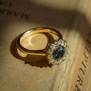 Teal sapphire engagement ring with oval gemstone and diamond cluster halo