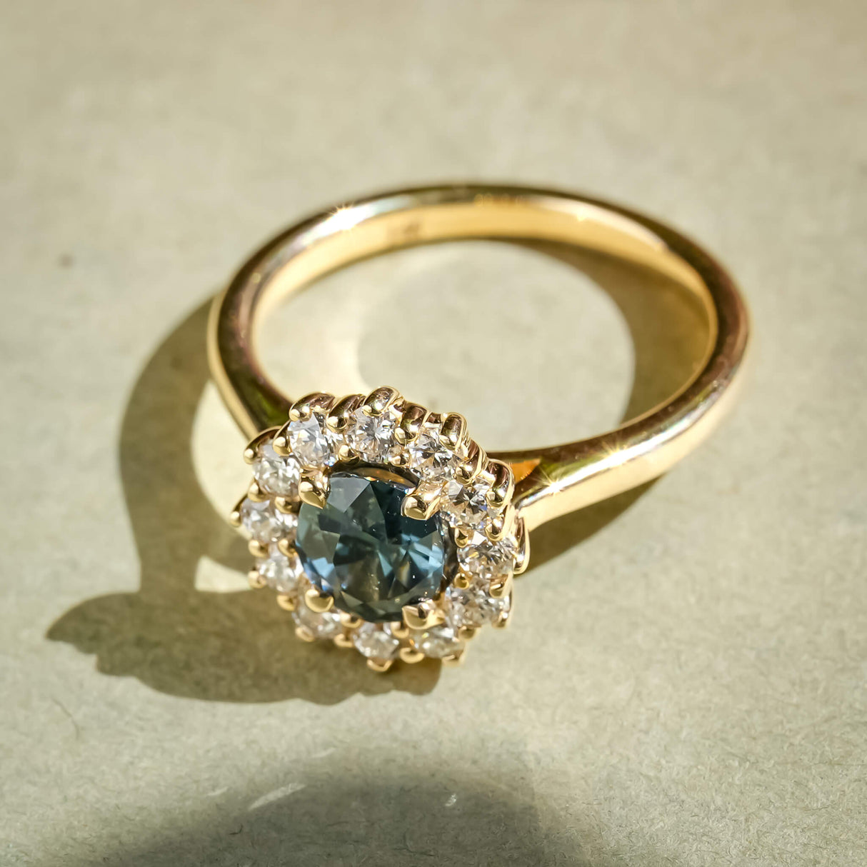 Teal sapphire and diamond cluster ring with oval center stone in gold band