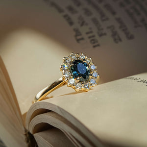 Teal sapphire ring with oval gemstone and diamond cluster halo in gold