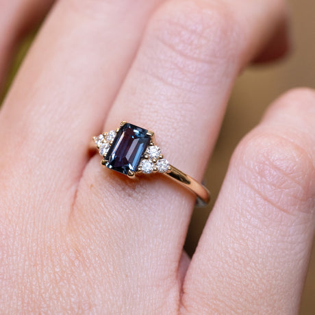 Teal sapphire and diamond cluster tre-foil engagement ring with rectangular teal sapphire and diamond detailing worn on finger.