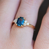 Teal sapphire centre stone with diamond trefoil cluster engagement ring as a close-up on a hand. 