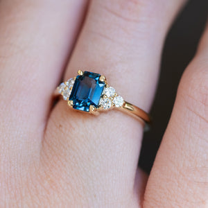 Teal sapphire centre stone with diamond trefoil cluster engagement ring as a close-up on a hand. 