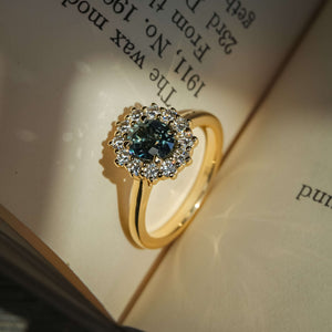 Teal sapphire engagement ring with oval gemstone and diamond cluster halo