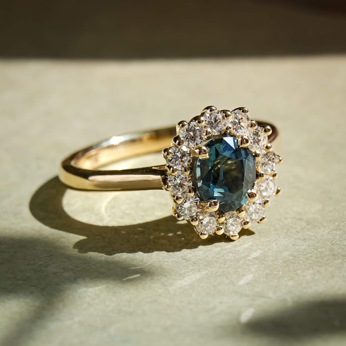 Oval teal sapphire surrounded by diamond cluster engagement ring
