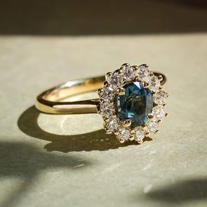 Oval teal sapphire surrounded by diamond cluster engagement ring