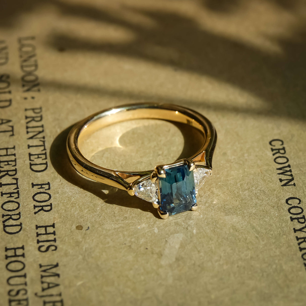 Teal sapphire and diamond three stone engagement ring in yellow gold band