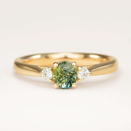 Teal sapphire and diamond three-stone engagement ring in yellow gold with round centre stone and diamond side stones.