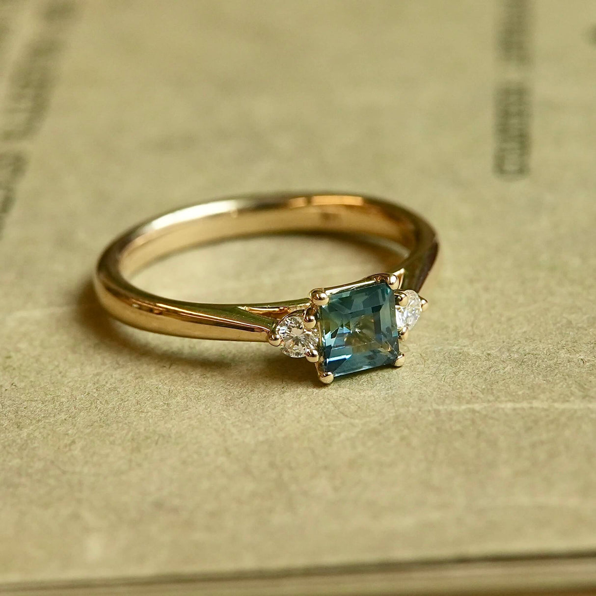 Teal sapphire and diamond three stone engagement ring in yellow gold