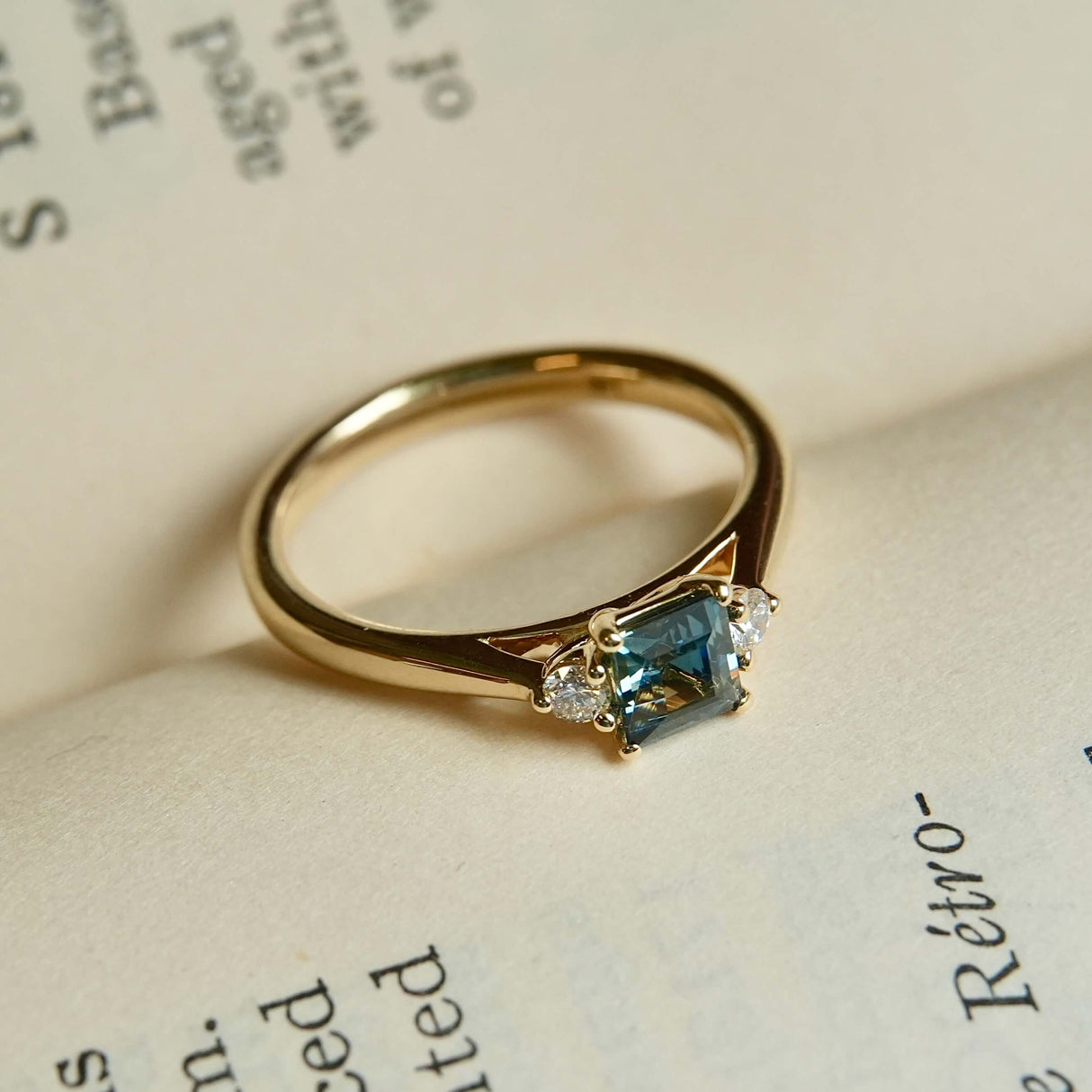 Teal sapphire engagement ring with diamond three stone setting in yellow gold