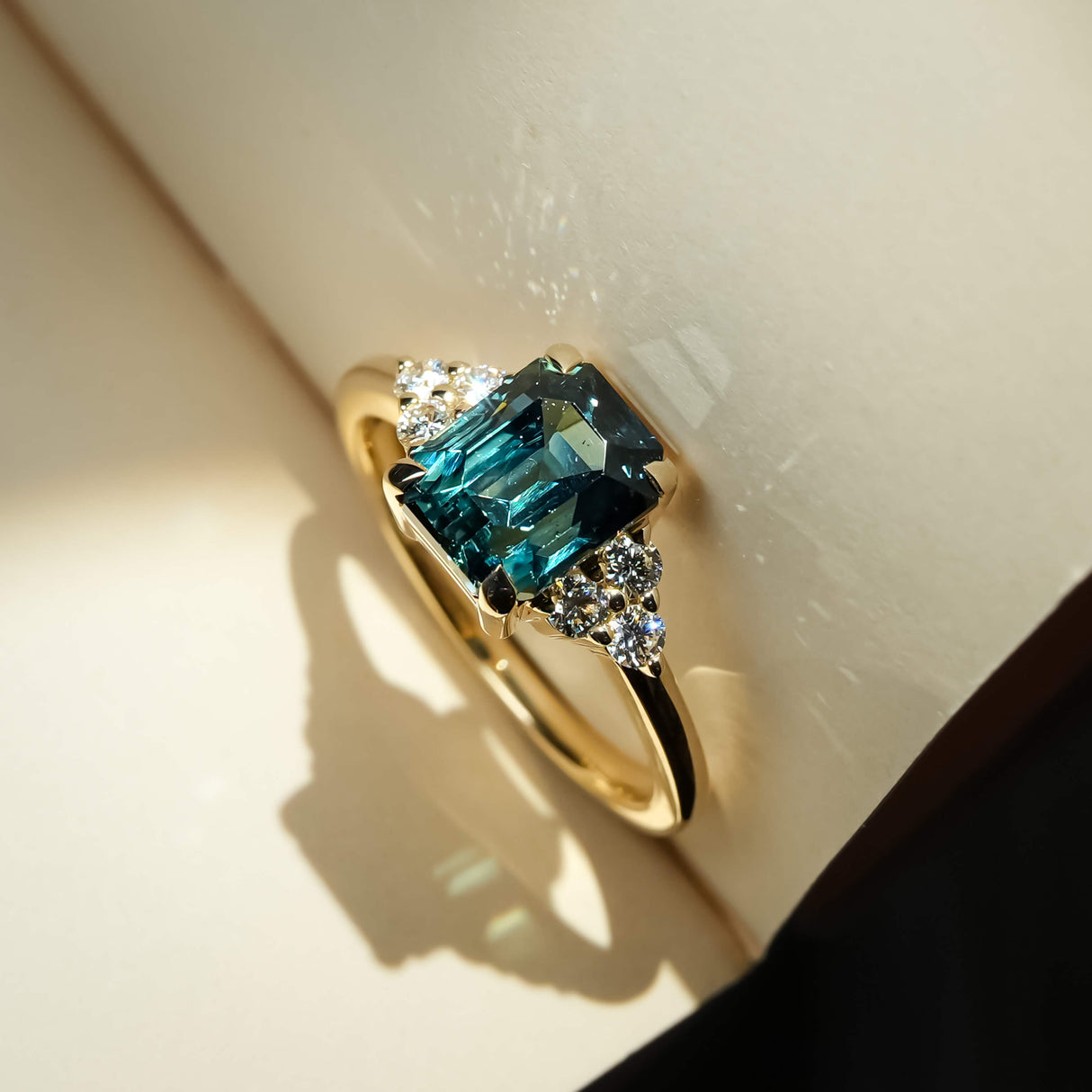 Teal sapphire engagement ring with emerald cut gemstone and diamond trefoil cluster