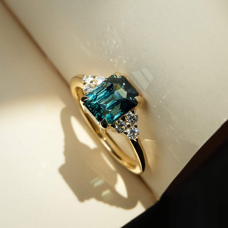 Teal sapphire engagement ring with emerald cut gemstone and diamond trefoil cluster