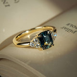 Teal sapphire engagement ring with emerald cut gemstone and diamond trefoil cluster