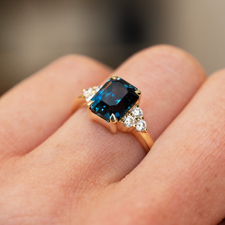 Sapphire and diamond ring highlighting central teal stone and trefoil style setting.