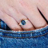 A hand wearing a ring with a teal sapphire on denim fabric.