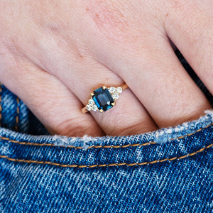 A hand wearing a ring with a teal sapphire on denim fabric.