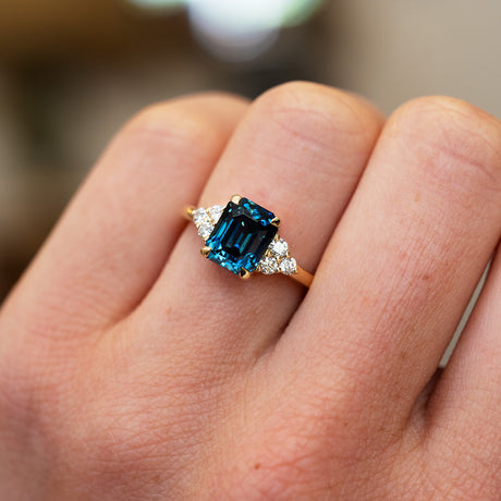 Teal sapphire ring with diamond side stones showing deep tones.