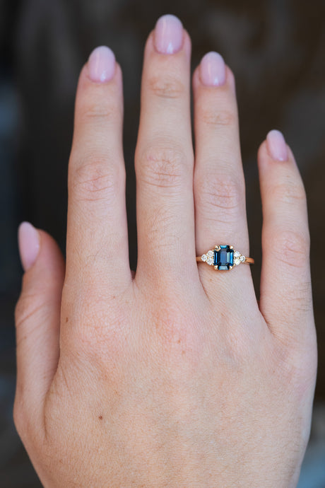 Teal sapphire and diamond trefoil engagement ring on a hand in yellow gold.