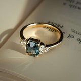 Teal sapphire engagement ring with emerald cut gemstone and diamond trefoil cluster