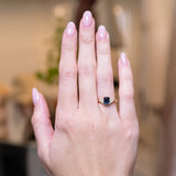 Teal sapphire and diamond cluster tre-foil engagement ring worn on hand with gold band.