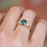 Teal sapphire and diamond cluster tre-foil engagement ring with polished gold band and diamond accents.