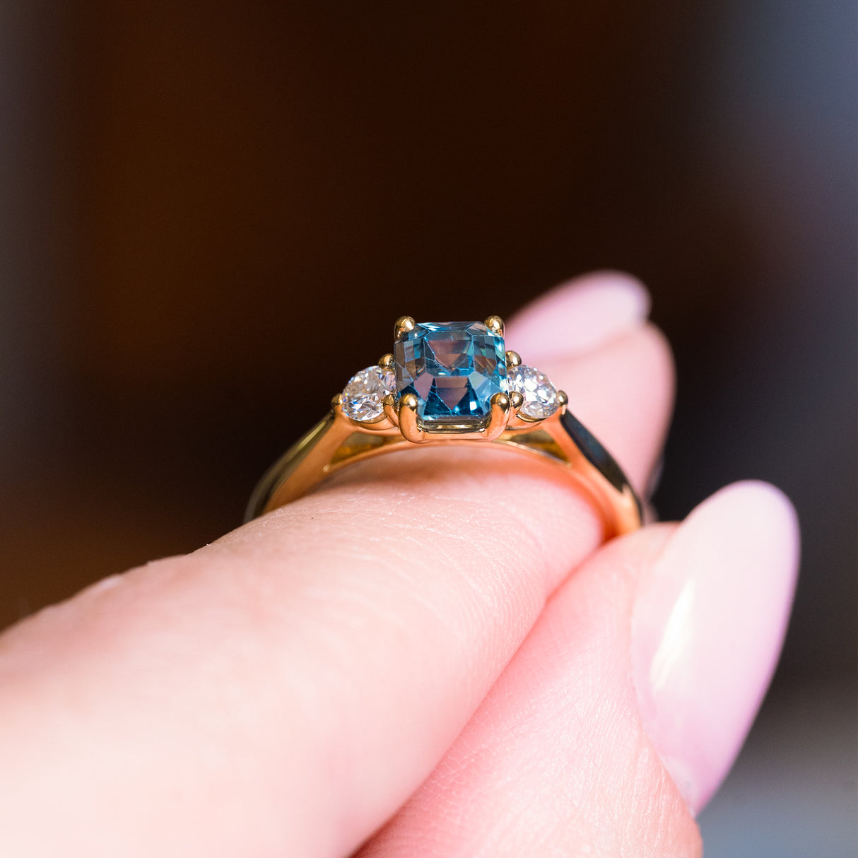 Teal sapphire and diamond three-stone engagement ring showing raised setting and gold band.
