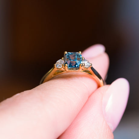 Teal sapphire and diamond three-stone engagement ring showing raised setting and gold band.