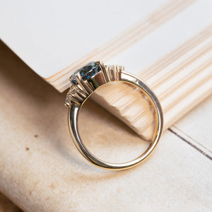 Teal sapphire and diamond cluster tre-foil engagement ring with open gallery setting and polished gold band.