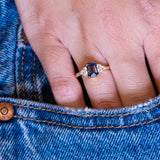 Teal sapphire and diamond cluster tre-foil engagement ring worn on hand with denim pocket styling.
