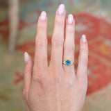 Teal sapphire and diamond cluster tre-foil engagement ring worn on hand with round teal sapphire centre stone.