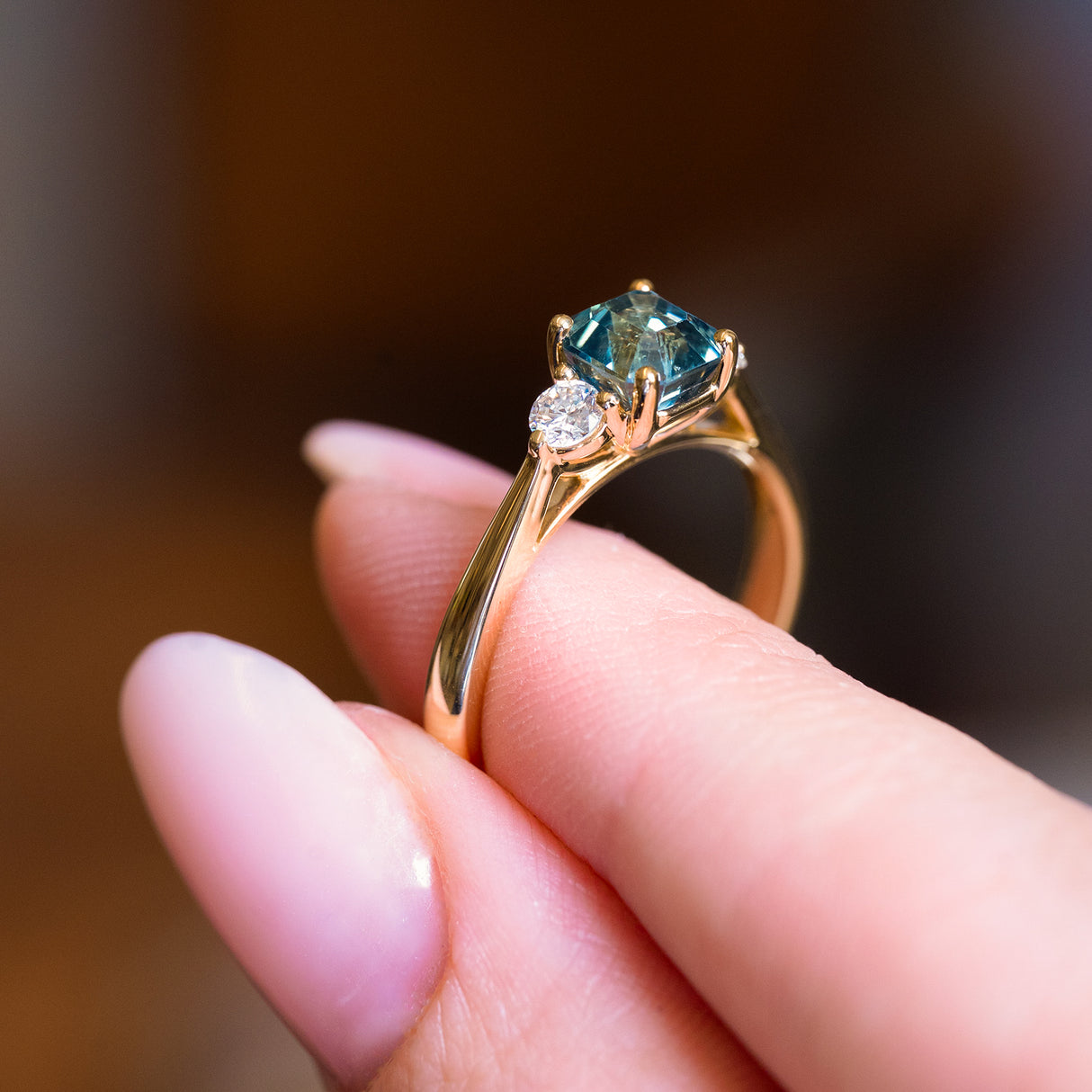 Teal sapphire and diamond three-stone engagement ring with sculpted gold setting and diamond accents.