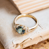 Teal sapphire and diamond cluster tre-foil engagement ring with round teal sapphire and diamond side stones.