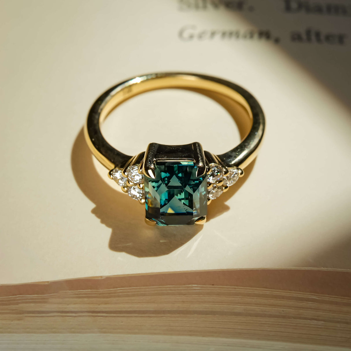 Teal sapphire ring with emerald cut gemstone and diamond trefoil cluster in gold