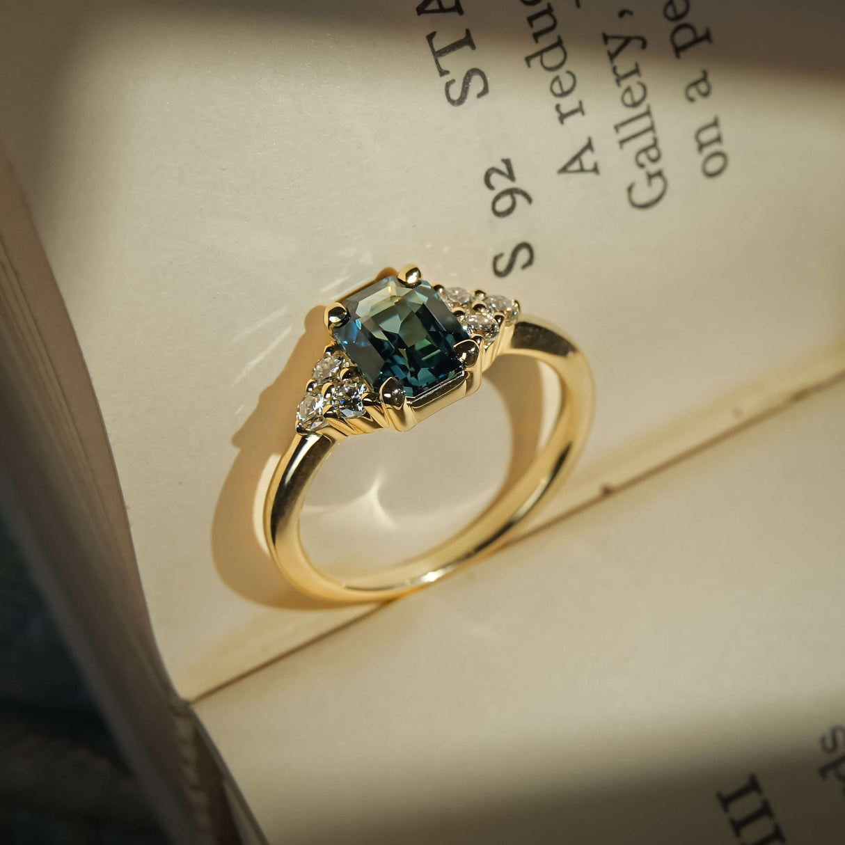 Teal sapphire ring with emerald cut gemstone and diamond trefoil cluster design