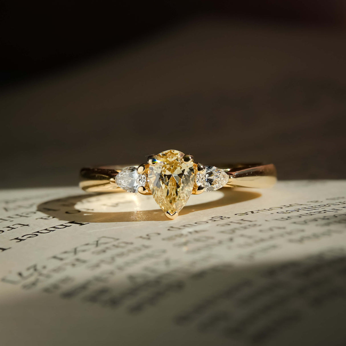 tinted yellow pear diamond three stone ring with diamond accents in yellow gold