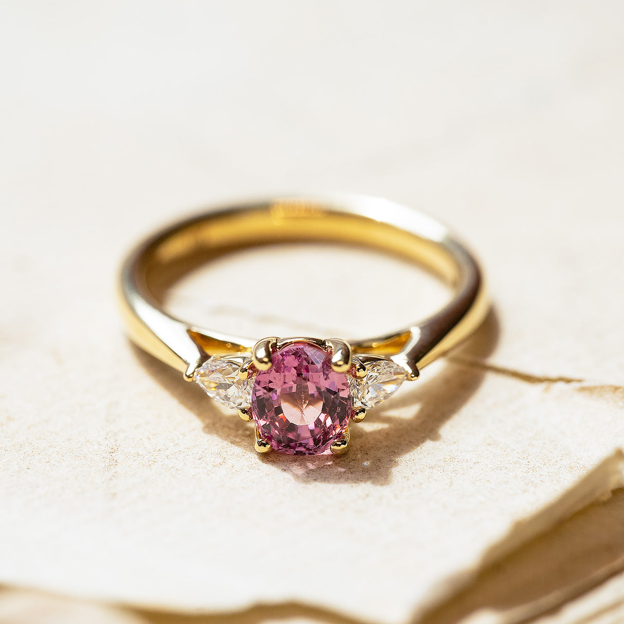 Pink sapphire and diamond three-stone engagement ring with oval-cut pink sapphire and gold band.