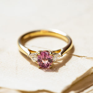 Pink sapphire and diamond three-stone engagement ring with oval-cut pink sapphire and gold band.
