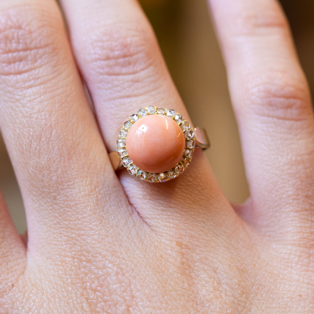 Close-up of a hand wearing a Victorian angel skin coral ring highlighting smooth coral cabochon and surrounding diamonds.