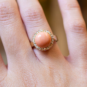 Close-up of a hand wearing a Victorian angel skin coral ring highlighting smooth coral cabochon and surrounding diamonds.