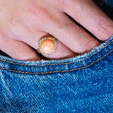 Close-up of a hand wearing a Victorian angel skin coral and diamond cluster ring with blue denim pocket detail.