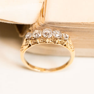 Victorian old-mine cut diamond five-stone ring showcasing a row of sparkling antique diamonds set above ornate engraved gold detailing.