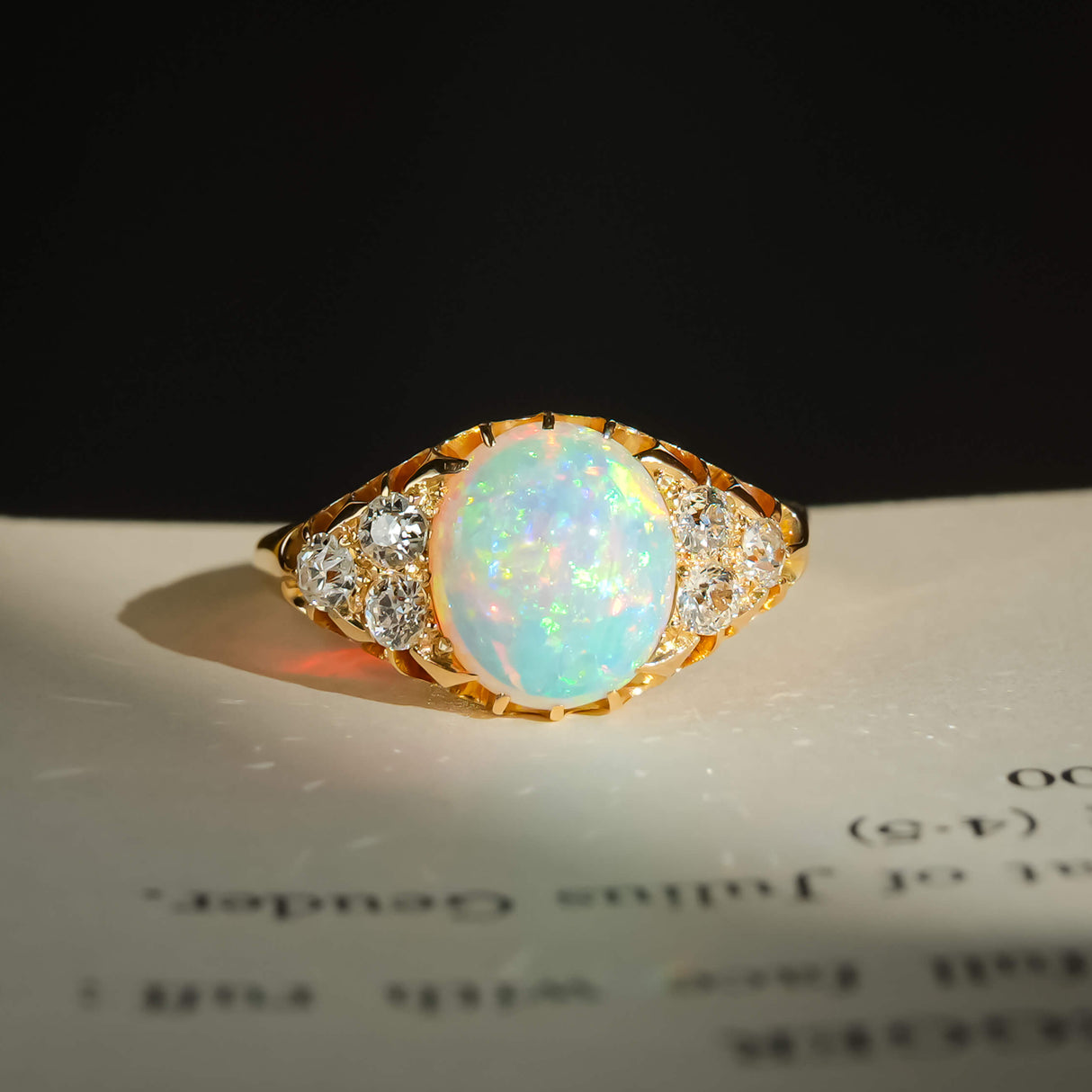 victorian cabochon opal diamond cluster ring with yellow gold band placed on a book in natural sunlight