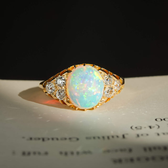 victorian cabochon opal diamond cluster ring with yellow gold band placed on a book in natural sunlight