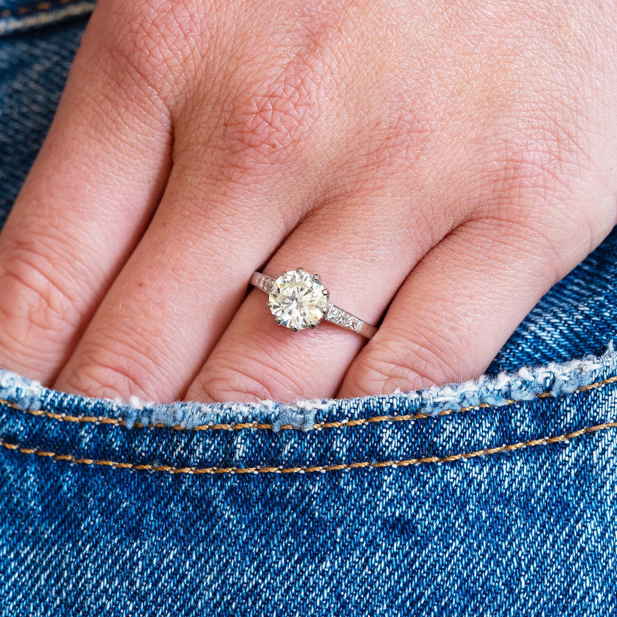 Close-up of a hand wearing a vintage diamond ring with a denim jeans pocket detail.